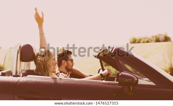 Happy couple making a tour in\
central italy. Driving on a convertible car in the italian\
countryside 