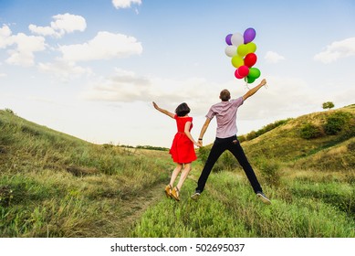 happy couple of man and woman in love, with colored balloons at sunset. The guy with the girl jumped from the balloons in hands