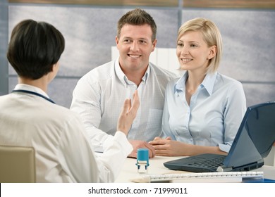 Happy Couple At Medical Appointment, Talking To Doctor, Smiling.?