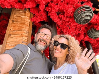 Happy couple middle age taking selfie picture with red flowers in background enjoying tourist vacation outdoor leisure activity in travel lifestyle. Cheerful man and woman sharing content online - Powered by Shutterstock