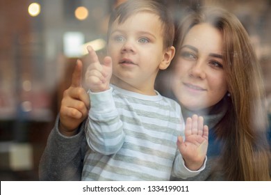 Happy Couple Of Mom And Child Boy. The Family Looks Through The Cafe Windows On The Street, The Mother Shows A Finger In The Window And The Son Watches. Selective Focus