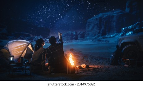 Happy Couple Nature Camping In The Canyon, Sitting Watching Campfire Together, Talking, Watching Night Sky. Two Traveling Young People On Inspirational Vacation Trip Marvel At Milky Way Stars