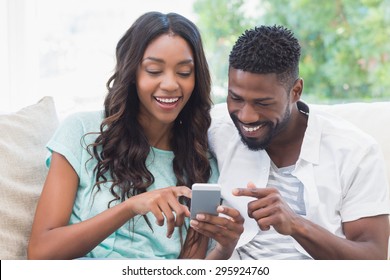 Happy Couple On The Couch Using Phone At Home In The Living Room