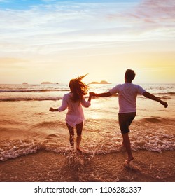 Happy Couple On Honeymoon Vacation Travel, Romantic Getaway Dream Beach Holidays, Happiness, Silhouettes Of Man And Woman Running To The Sea At Sunset Together