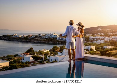 Happy couple on vacation time enjoys the summer sunset over the Aegean Sea by the swimming pool with an aperitif drink