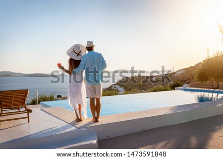 Happy couple on vacation time enjoys the summer sunset by the pool with an aperitif drink