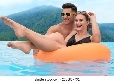 Happy couple in outdoor swimming pool at luxury resort with beautiful view of mountains - Powered by Shutterstock