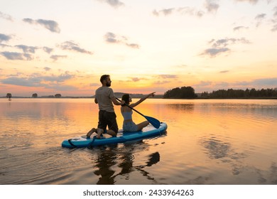 Happy couple paddle boarding at lake during sunset together. Concept of active family tourism and supping. aesthetically wide shot. - Powered by Shutterstock