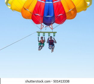 Happy couple Parasailing in Dominicana beach in summer. Couple under parachute hanging mid air. Having fun. Tropical Paradise. Positive human emotions, feelings, joy.