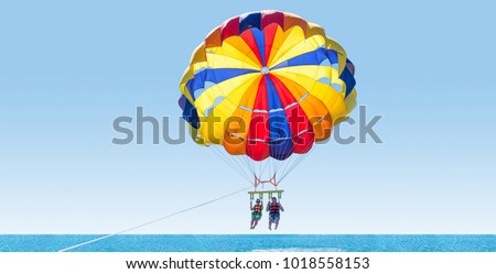 Happy couple Parasailing on Tropical Beach in summer. Couple under parachute hanging mid air. Having fun. Tropical Paradise. Positive human emotions, feelings, family, travel, vacation.