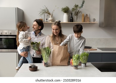 Happy couple of parents and kids unpacking shopping grocery paper bag in kitchen, producing organic food, fresh vegetables, green lettuce, spinach, caring for healthy eating. Family nutrition concept - Powered by Shutterstock