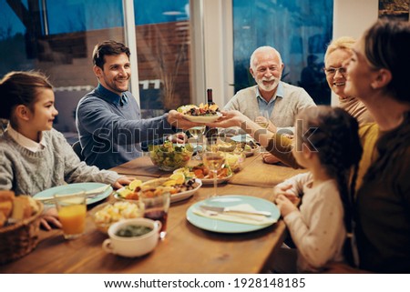 Happy couple passing food while having family lunch in dining room. 