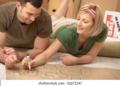 Happy couple planning to furniture the new house after moving in  girl drawing and marker paper 