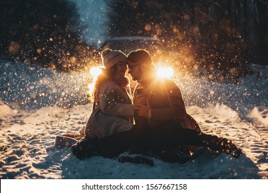 Happy Couple Playful Together During Winter Holidays Vacation Outside In Snow Park At Night Time With Car`s Ligths On Background.