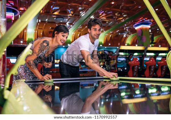 Happy couple playing coin operated air hockey game as a team in a gaming arcade. Friends having fun playing air hockey in a gaming parlour.