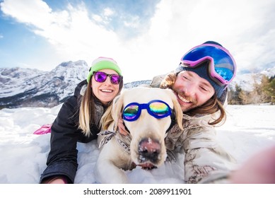 Happy couple playing and having fun with their loyal dog in the snow