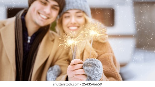 A happy couple poses outdoors, holding sparklers while enjoying a snowy winter day. They are bundled in warm clothing and smiling, surrounded by a serene, white landscape. - Powered by Shutterstock