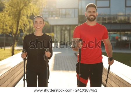 Happy couple practicing Nordic walking with poles outdoors on sunny day