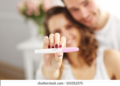 Happy couple with pregnancy test in bedroom