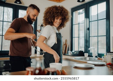 Happy couple prepares a meal together in a modern kitchen, smiling and enjoying the moment of partnership. Ingredients cover the counter, creating a cozy atmosphere of love and togetherness - Powered by Shutterstock