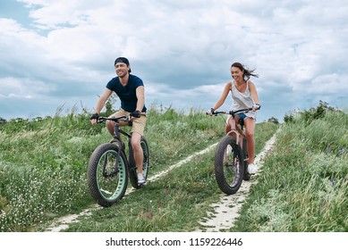 Happy Couple Racing On A Fat Bike Along The Sand And Grass High In The Mountains. 