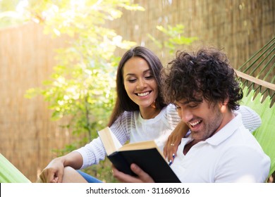 Happy Couple Reading Book On Hammok Outdoors