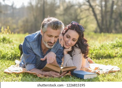 Happy Couple Reading A Book Together Outdoors