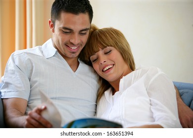 Fröhliches Paar, das eine Zeitschrift auf einem Sofa liest