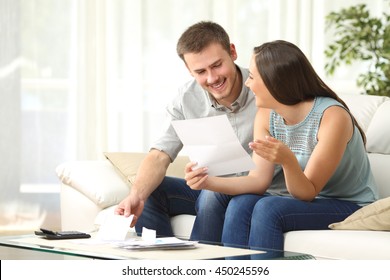 Happy Couple Reading Mail And Checking Accountancy Looking Each Other Sitting On A Couch At Home