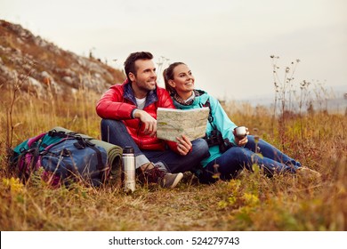Happy couple reading map and drinking tea during fall, autumn hike