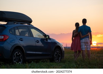 Happy couple relaxing beside their SUV car during honeymoon road trip at sunset. Young man and woman enjoying time together travelling by vehicle. - Powered by Shutterstock