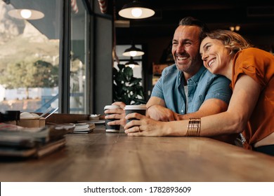 Happy couple relaxing at cafe with a cup of coffee. Smiling man and woman sitting at coffee shop and looking outside the window together.