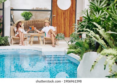 Happy couple relaxing in chaise-lounges by swimming pool and enjoying delicious fruit cocktails - Powered by Shutterstock