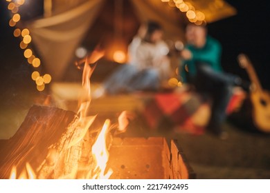 Happy couple relaxing in glamping on autumn evening, drinking wine and playing guitar near cozy bonfire. Luxury camping tent for outdoor recreation and recreation. Lifestyle concept - Powered by Shutterstock