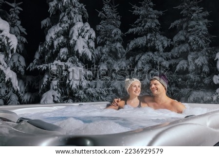 happy couple relaxing in outdoor hot tub at winter in resort spa hotel. romantic getaway