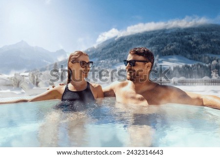 happy couple relaxing in outdoor hot tub at ski spa resort. winter vacation