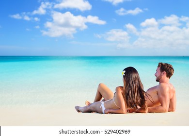 Happy Couple Relaxing Sun Tanning On Vacation Beach Lying Down On White Sand Looking At Ocean Copyspace Background. Sunbathing On Holiday.