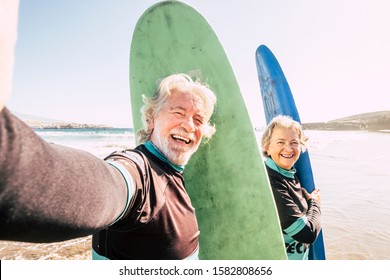 happy couple of seniors at the beach trying to go surf and having fun together - mature woman and man married taking a selfie with the wetsuits and surftables with sea or ocean at the background - Powered by Shutterstock