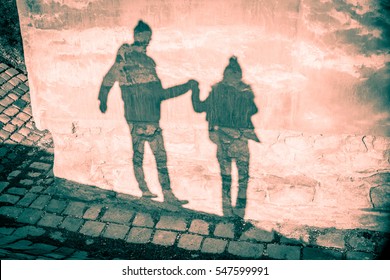 Happy couple shadow silhouettes in winter clothing holding their hands and walking against grunge old mauve pink wall and stone pavement background - Saint Valentine Day card backdrop - Powered by Shutterstock