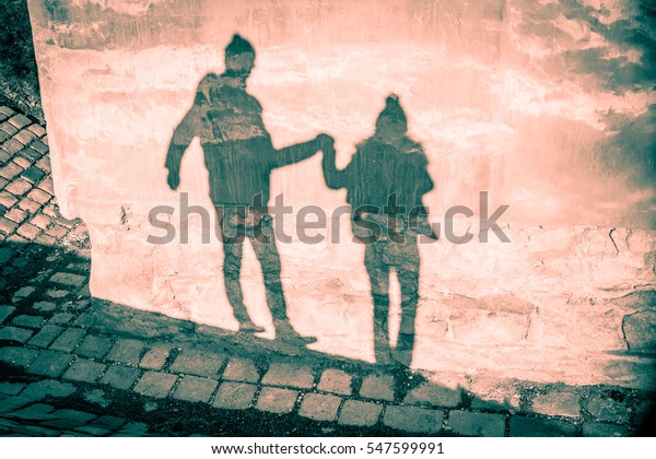 Happy couple shadow silhouettes in winter clothing holding their hands and walking against grunge old mauve pink wall and stone pavement background. 