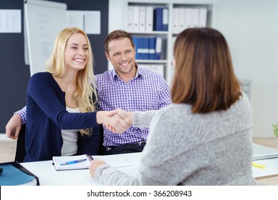 Happy couple shaking hands with a female business broker or investment adviser as they attend a meeting in her office