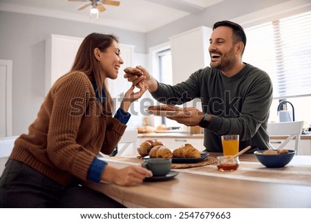 Happy couple sharing breakfast while eating in their kitchen. Focus is on man. 