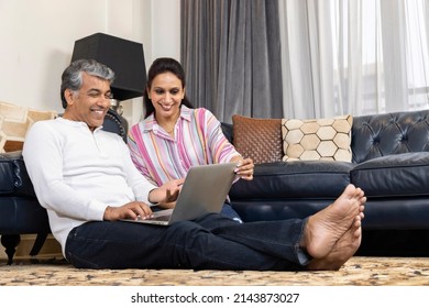 Happy couple sharing media content using laptop sitting on floor at home