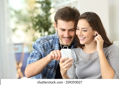 Happy couple sharing music from smart phone sitting on a couch at home - Powered by Shutterstock