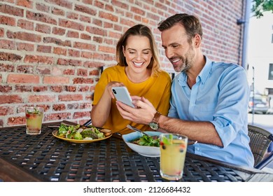 Happy couple sharing smartphone while out in the city eating lunch at outdoors cafe - Powered by Shutterstock