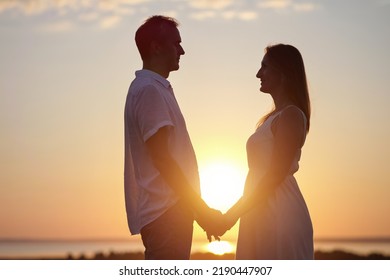 Happy Couple Silhouettes Stand Showing Pure Love To Each Other In Back Lit. Wife And Husband Enjoy Being Together And Stand On Meadow At Orange Back Sunset Side View