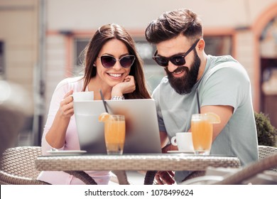 Happy couple sitting in cafe with coffee,looking at laptop,smiling and drink juice.