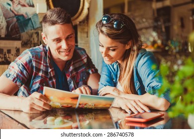 Happy Couple Sitting In Cafe And Looking At Menu