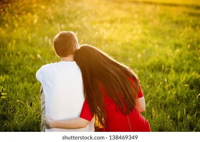 Happy couple is sitting in grass watching sunset