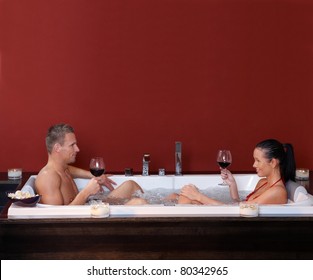 Happy couple sitting in jacuzzi together, drinking red wine, smiling.?